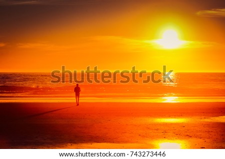 Man in silhouette standing on the beach at sunset