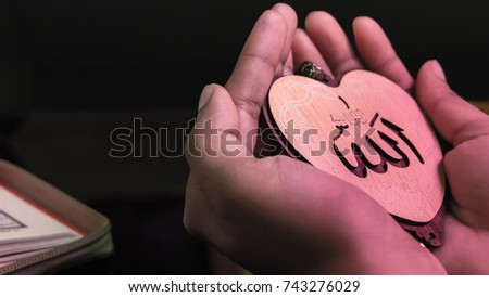Hands up for prying, holding heart(Love) shaped tag written in Arabic "Allah" English meaning of God. Royalty-Free Stock Photo #743276029