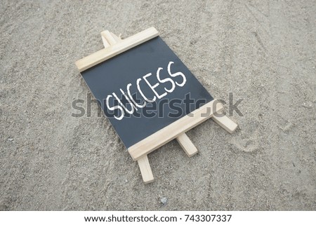 mini black board written success concept over sand background