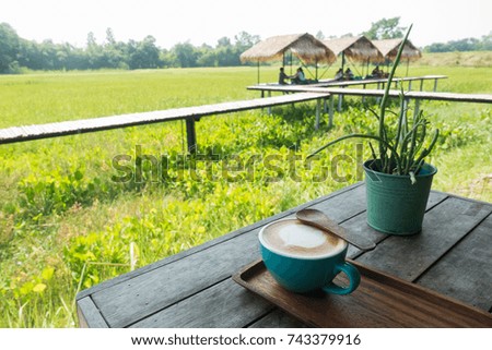 Selective focus picture of a cup of late coffee and spoon on wooden table with organic green terraced rice field