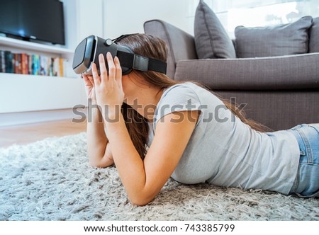 Young woman using virtual reality glasses at home, female wearing VR headset