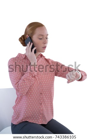 Young female executive looking at wristwatch while talking on mobile phone