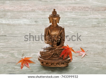 Buddha  statue  with japan maple leaves on wooden background 