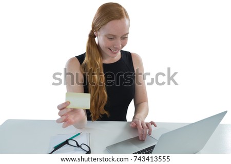 Young female executive holding visiting card while using laptop