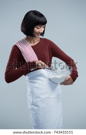 Smiling female chef mixing flour in bowl with whisk against white background