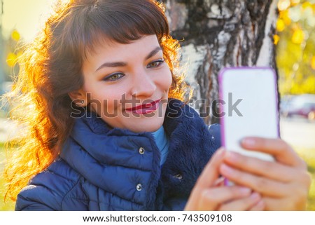 beautiful woman is taking pictures on the phone in an autumn park