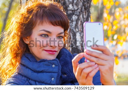 beautiful woman is taking pictures on the phone in an autumn park