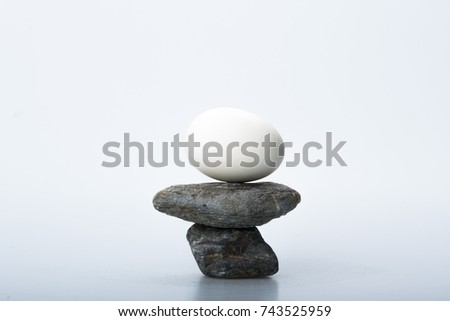 Egg balanced on top of stack of stones isolated on white with copy space. Zen design concept