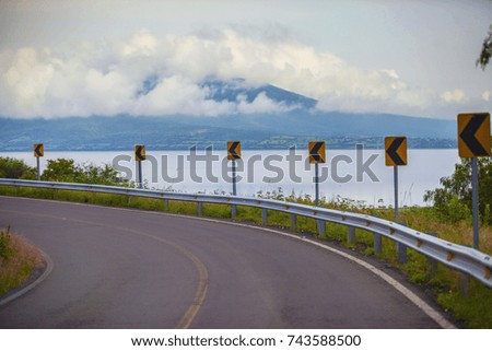 road turning to the left with a beautiful lake and mountains cloudy background