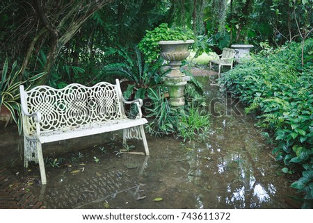 White chair in waterlogged outdoor garden, full of trees and bushes. Royalty-Free Stock Photo #743611372