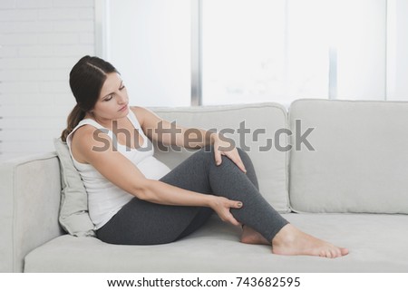 A pregnant woman sits at home on a light sofa. Her legs are numb and she rubs them. Unpleasant for her.