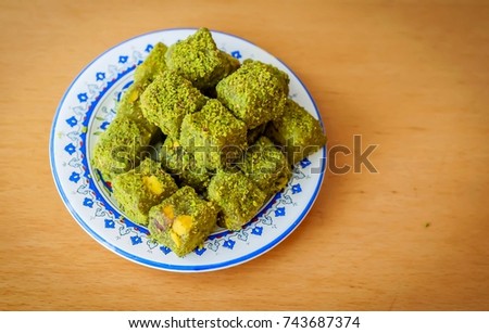 Powder coated pistachio Turkish delight ("rahat lokum" or "lokum") on a decorated plate on a wooden table stock image.