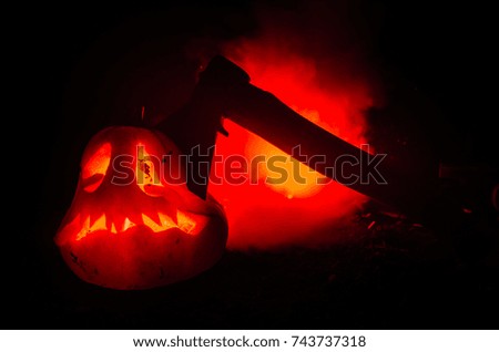 Scary orange pumpkin with carved eyes and a smile with burning candles and an ax on a dark background with fire sky. For the Halloween party. Empty space. Selective focus