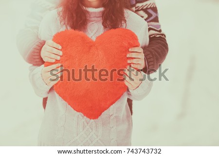 Young couple wearing sweaters with heart hugging outdoors in winter. Vintage color
