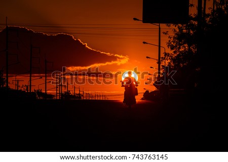 The silhouette of a motorcycle driver on a street in the sunset.