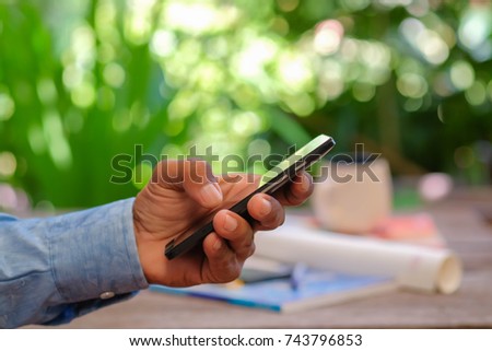a selective focus picture of a cellphone in a hand with working table and green blur background 