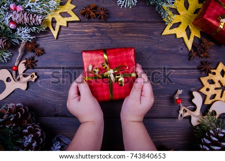 Christmas or new year wooden background framed with season decoration. Winter holiday theme. Baby hands hold a gift