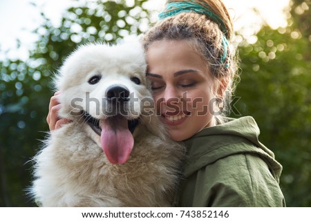 young woman in green coat and multicolored dreadlocks with her white Samoyed dog posing for a picture with closed eyes in autumn Park