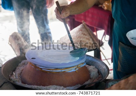 Thai local cooking direction steam big local noodle pour flour dissolve with water by stainless dipper on the straining cloth over the water in clay pot put the clay pot on the big pan over the oven