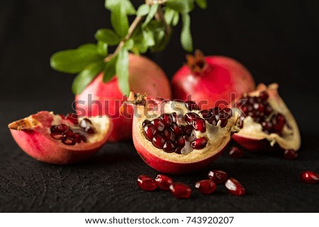 Closeup of ripe pomegranate fruits and seeds over a textured black background