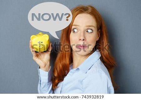 Financial theme of surprised red-haired young woman holding piggy bank