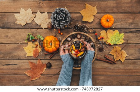 Hands holding Delicious cup of tea on a rustic wooden table. Autumn composition
