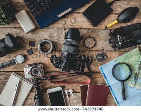top view travel concept and photographer work space with action camera, digital camera, smartphone, map and  camera accessory on wooden background, Tourist essentials.