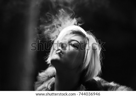 Blond woman smoking cigarette at night and looking up black and white