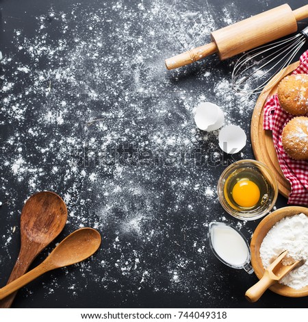 Baking ingredients. Bowl, eggs, flour, eggbeater, rolling pin and eggshells on black chalkboard from above.