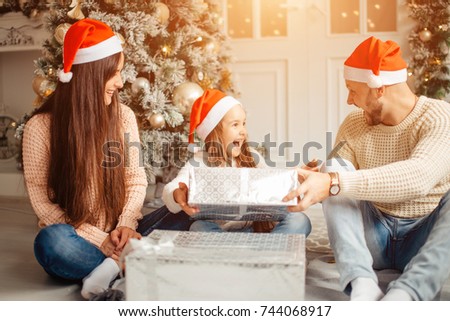 Merry Christmas and Happy Holidays. Cheerful cute little child girl surprised with present. Kid holds a gift box near Christmas tree indoors.