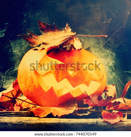 Burning Halloween pumpkin lantern head jack with leaves on wooden background toned