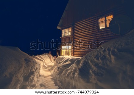 active rest in the mountains in winter. the view from the outside is a night starry sky and the view of the house is light from the windows, drifts large wooden house for tourism and a satellite dish