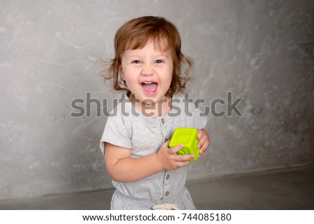 Little girl playing with toy on gray wall background. Kindergarten.