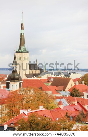 St. Olaf's Church and Buildings of Old Town Tallinn, Estonia. Colorful historic buildings with red tile rooftops, scenic cityscape panorama with autumn tree leaves. Empty sky background copy space.
