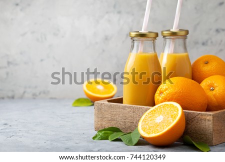 orange juice in glass bottles, fresh oranges in a wooden tray (box) on a gray concrete background Royalty-Free Stock Photo #744120349