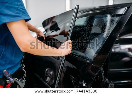 Male specialist applying car tinting film Royalty-Free Stock Photo #744143530