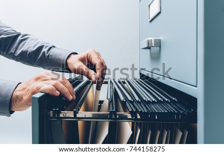 Office clerk searching for files into a filing cabinet drawer close up, business administration and data storage concept Royalty-Free Stock Photo #744158275