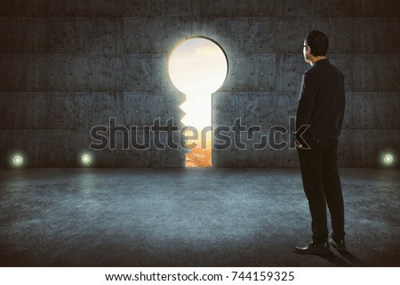 Hesitant businessman looking outside against concrete wall with key shaped door .