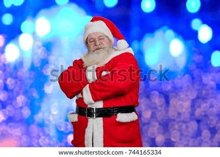 Brightful photo of realistic Santa Claus. Ola Santa Claus with crossed arms standing on blue shiny background. Santa Claus and New Year celebration.
