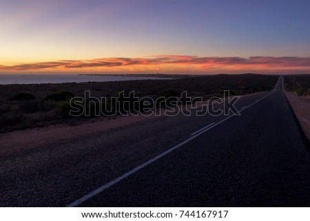 Desert concrete road during the sunset in Western Australia, with Dehnam city and harbour in the background.