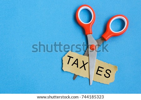Scissor cutting the word 'taxes' in a piece of paper. Royalty-Free Stock Photo #744185323