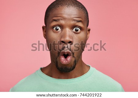 Portrait of shocked black male says wow, looks bugged eyes and rounded mouth, being amazed to see something unexpected. Terrified Afro American guy with surpised expression. Emotions concept Royalty-Free Stock Photo #744201922