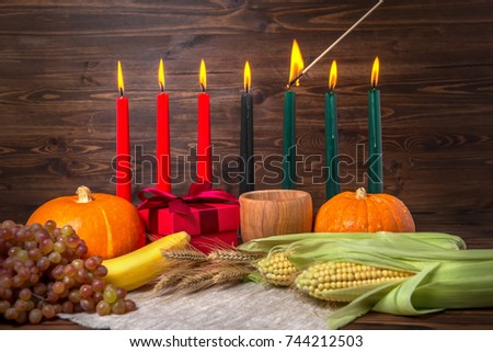 ignition of Kwanzaa traditional candles, festival concept with gift box, pumpkins, ears of wheat, grapes, corns, banana, bowl and fruits on wooden background, close up