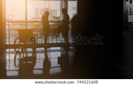 Blur hospital image, Silhouette woman using mobile phone in front of window terrace near wheelchair and chubby man, Guy waiting girlfriend talking with phone near lift, Sunset effect, Black copy space