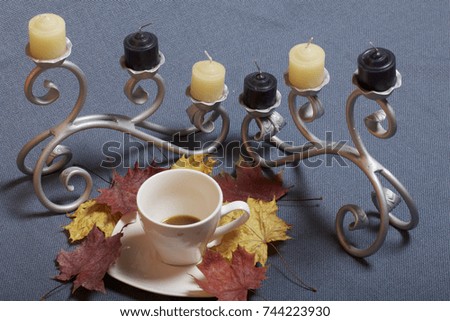 Forged metal candlestick with candles. A cup with unapproved coffee. Fallen autumn leaves of yellow and red are scattered on the surface.