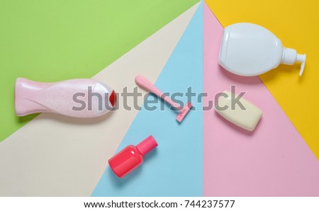 Products for the care of body, hair and personal hygiene on a multi-colored paper background. A bottle of fragrant perfume, lotion, shampoo, soap, razor. Top view. Trend of minimalism. Flat lay.