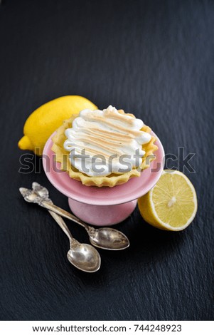 Tartlet with Italian meringue and lemon curd on a cakes stand on black slate background closeup