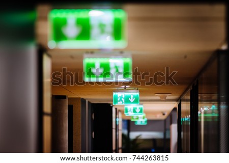 Row of green exit signs pointing to escape door in a modern office office Royalty-Free Stock Photo #744263815