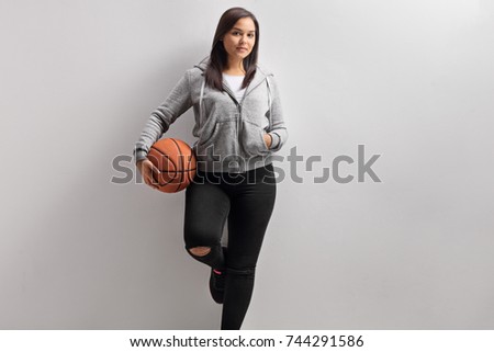 Teenage girl with a basketball leaning against a wall and looking at the camera