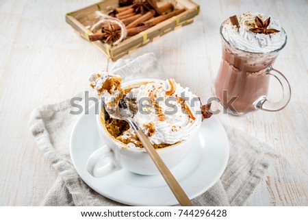 Recipes with pumpkins, fast food, microwave meal. Spicy pumpkin pie in mug, with whipped cream, ice cream, cinnamon, anise. On white wooden table, with cup of hot chocolate. Copy space